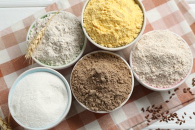 Photo of Different types of flour in bowls, spike and flaxseeds on table, flat lay