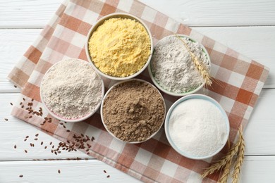Photo of Different types of flour in bowls, spikes and flaxseeds on white wooden table, flat lay
