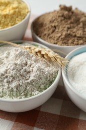 Photo of Different types of flour in bowls and spike on table, closeup