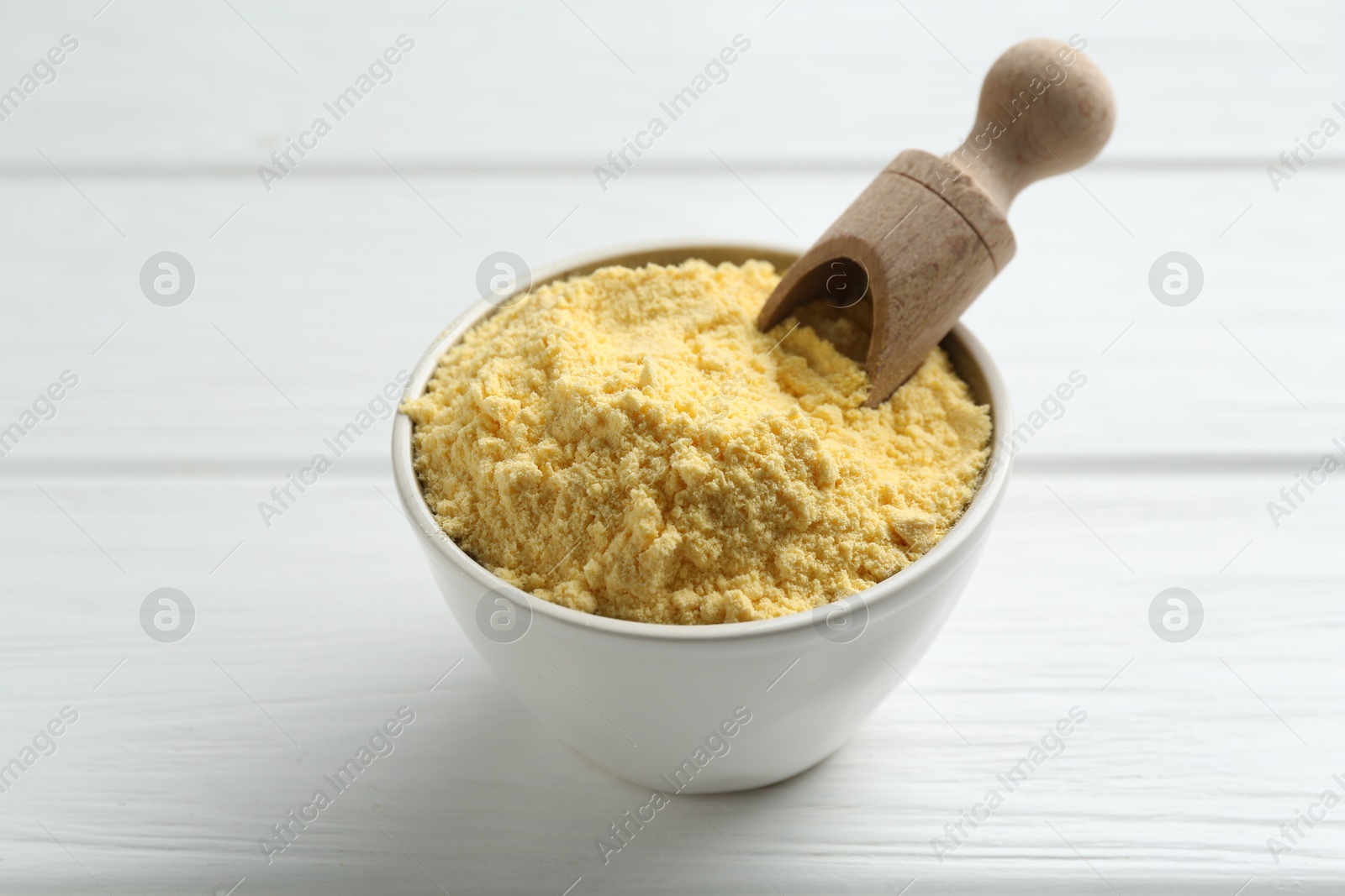 Photo of Corn flour in bowl and scoop on white wooden table, closeup