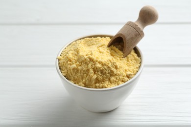 Photo of Corn flour in bowl and scoop on white wooden table, closeup
