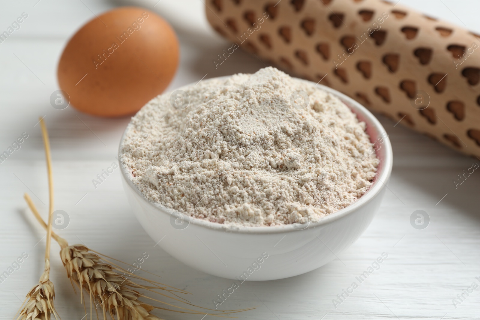 Flour in bowl, rolling pin, egg and spikes on white wooden table, closeup Photo of Flour in bowl, rolling pin, egg and spikes on white wooden table, closeup