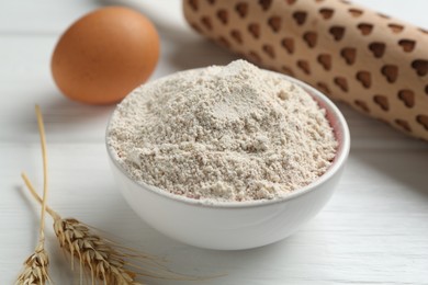 Photo of Flour in bowl, rolling pin, egg and spikes on white wooden table, closeup