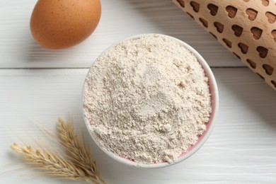 Photo of Flour in bowl, rolling pin, egg and spikes on white wooden table, flat lay
