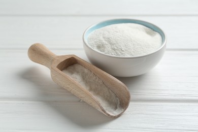 Photo of Flour in bowl and scoop on white wooden table, closeup