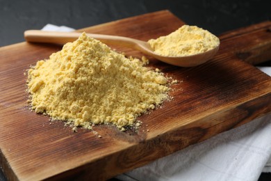 Photo of Pile of corn flour and spoon on black table, closeup