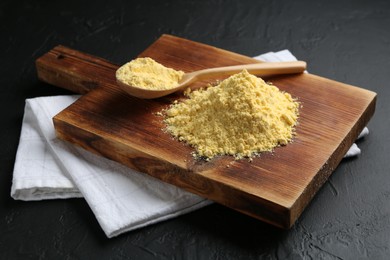 Photo of Pile of corn flour and spoon on black textured table, closeup