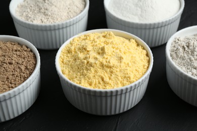 Photo of Different types of flour in bowls on black table, closeup