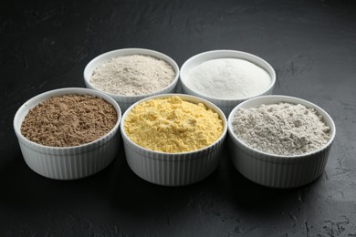 Photo of Different types of flour in bowls on black textured table, closeup