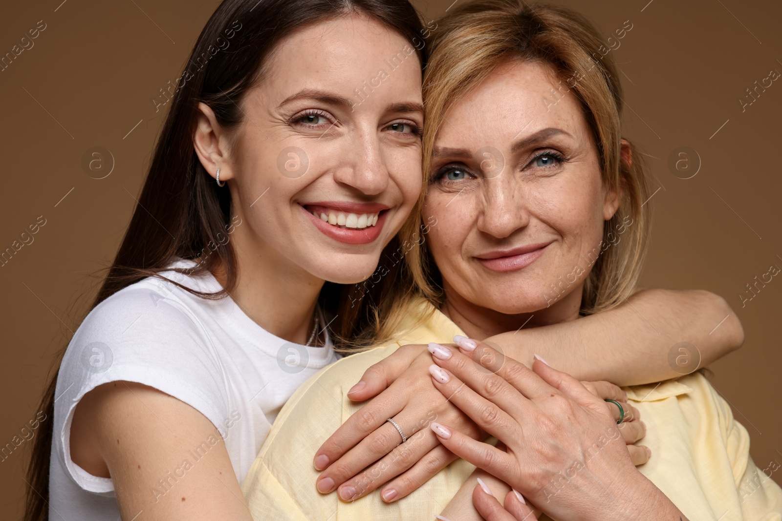 Woman hugging her mother on light brown background Photo of Woman hugging her mother on light brown background