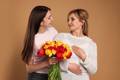 Photo of Woman giving her mother flowers on beige background