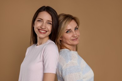 Photo of Cheerful mother and daughter back to back on beige background