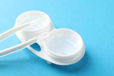 Photo of Contact lenses in case and tweezers on light blue background, closeup