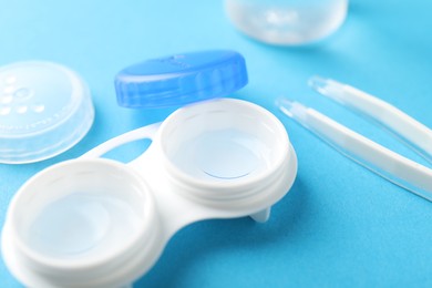 Photo of Contact lenses in case and tweezers on light blue background, closeup