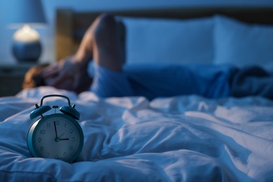 Photo of Frustrated man suffering from insomnia on bed indoors, focus on alarm clock