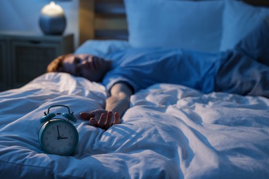 Photo of Frustrated man suffering from insomnia on bed indoors, focus on alarm clock