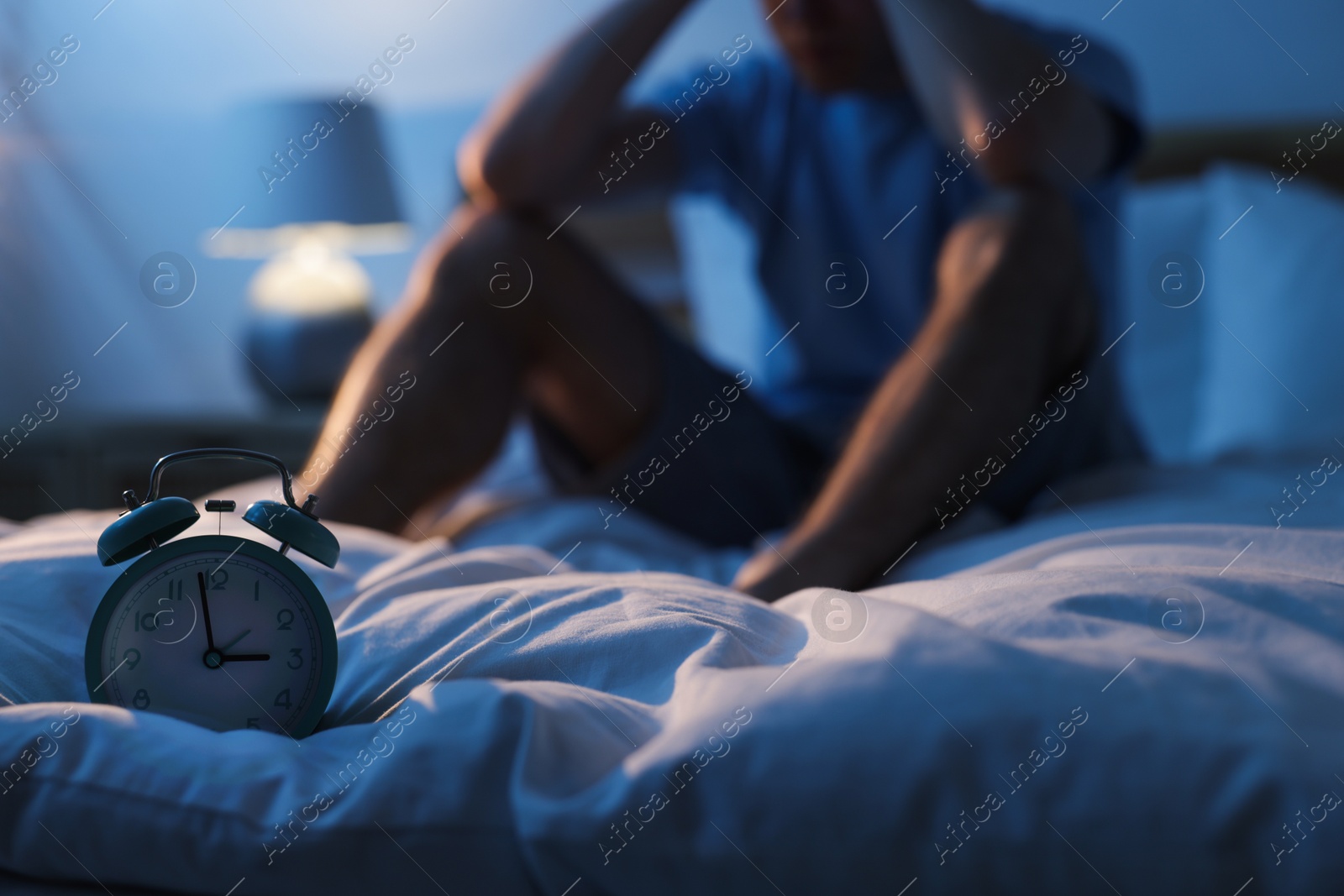 Frustrated man suffering from insomnia on bed indoors, focus on alarm clock Photo of Frustrated man suffering from insomnia on bed indoors, focus on alarm clock