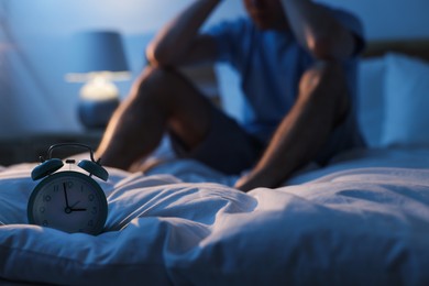 Photo of Frustrated man suffering from insomnia on bed indoors, focus on alarm clock
