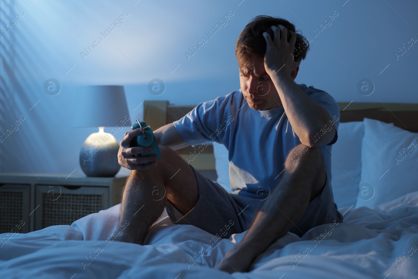 Frustrated man looking at alarm clock on bed at night. Insomnia problem Photo of Frustrated man looking at alarm clock on bed at night. Insomnia problem