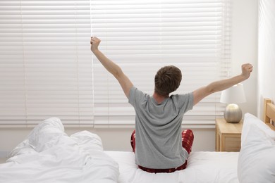 Photo of Man stretching on bed indoors, back view. Good morning