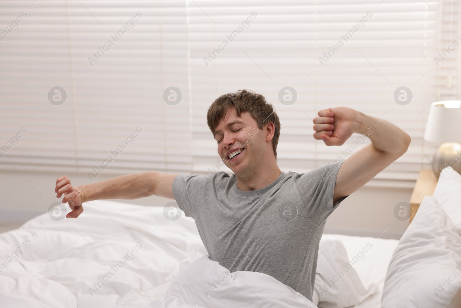 Happy man stretching in bed indoors. Good morning Photo of Happy man stretching in bed indoors. Good morning