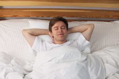 Photo of Young man sleeping in bed at home, top view