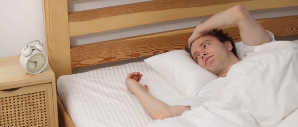 Photo of Overslept man looking at alarm clock in bed indoors