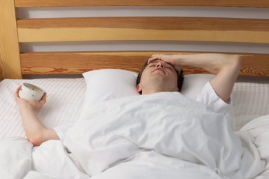 Photo of Overslept man with alarm clock in bed indoors