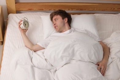 Photo of Overslept man with alarm clock in bed indoors