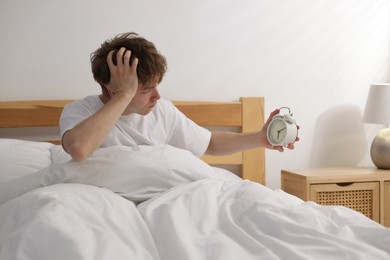 Photo of Overslept man looking at alarm clock in bed indoors