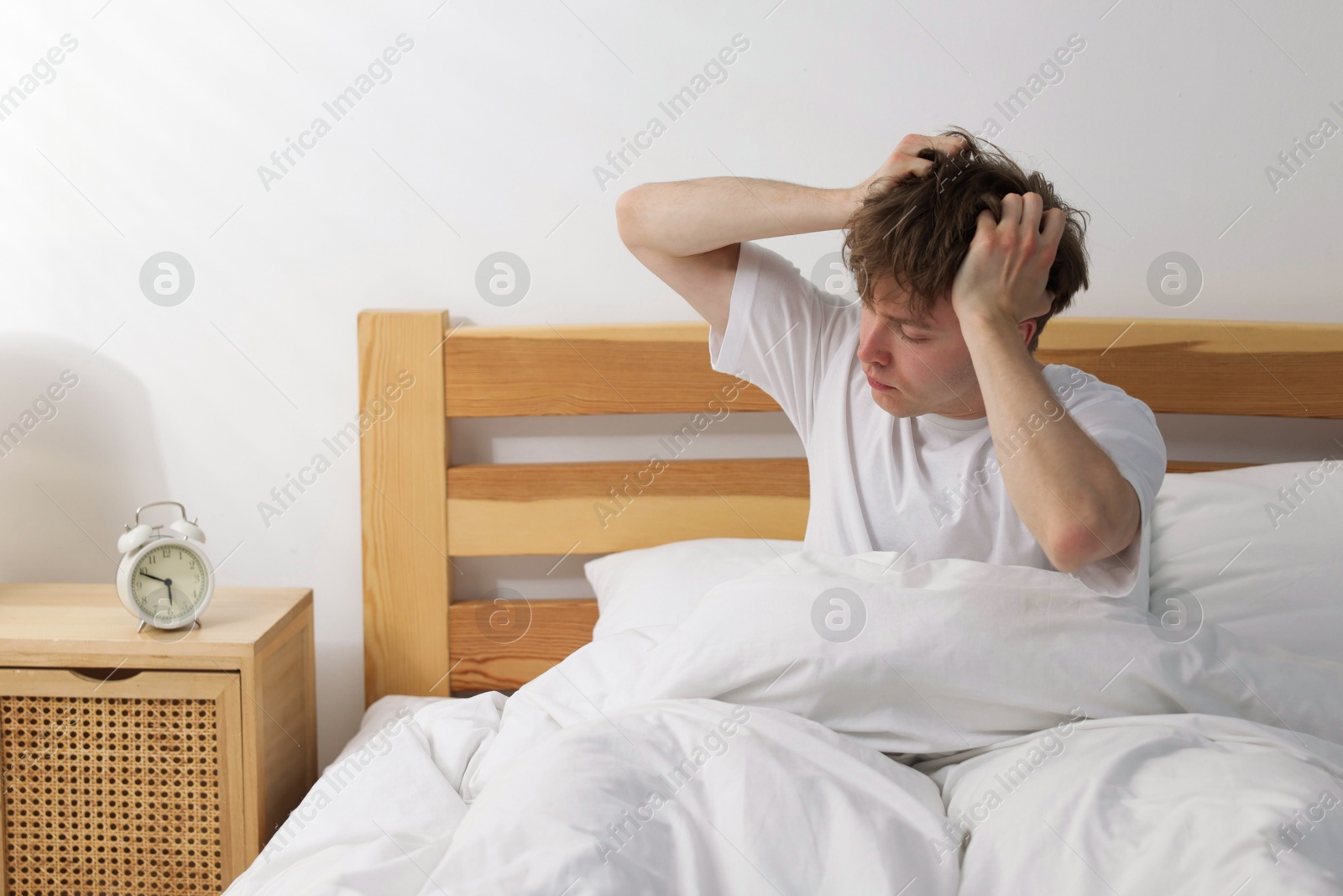 Overslept man looking at alarm clock in bed indoors Photo of Overslept man looking at alarm clock in bed indoors