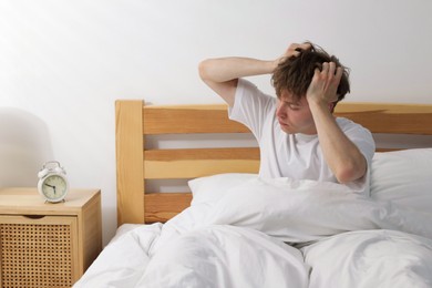 Photo of Overslept man looking at alarm clock in bed indoors