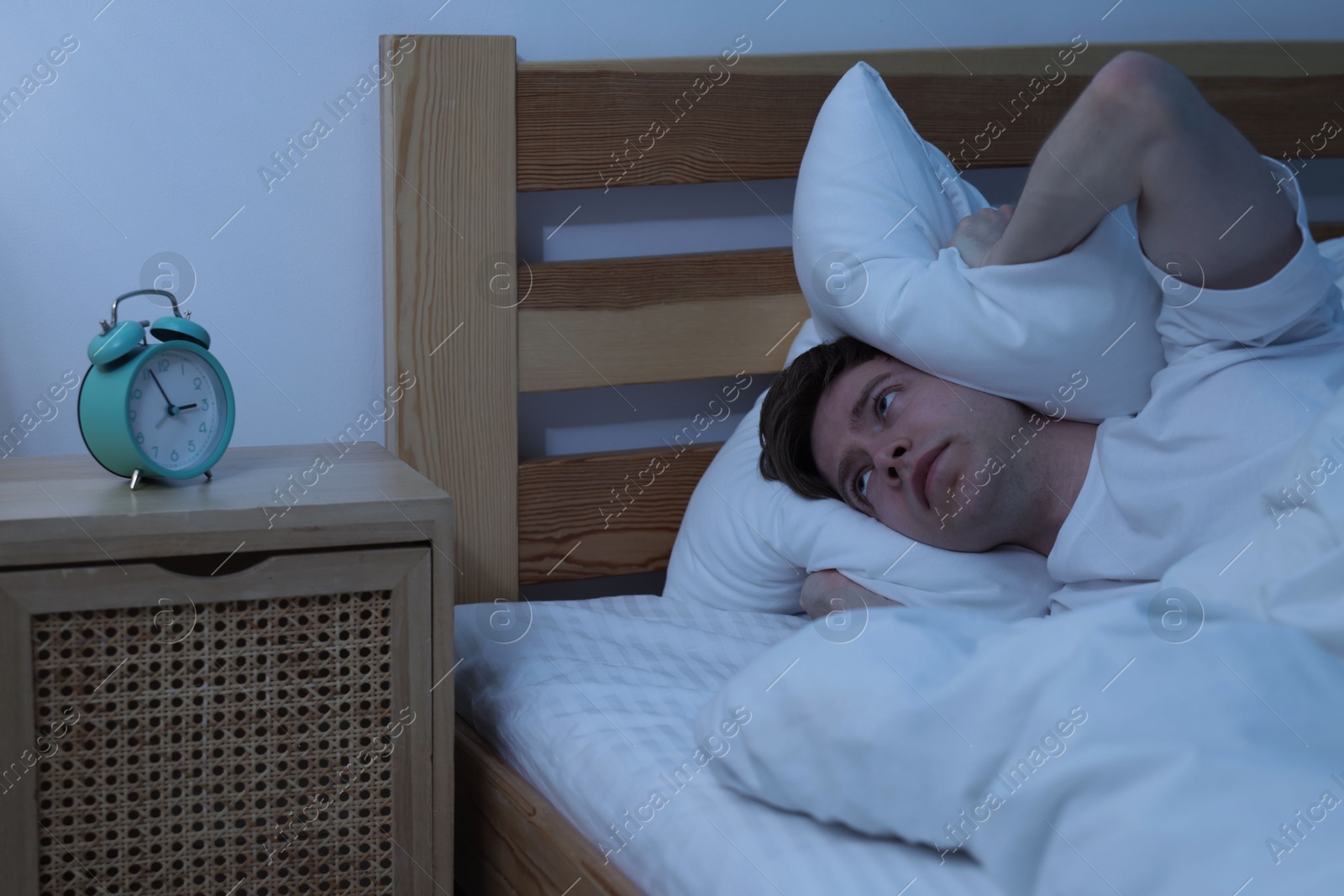Frustrated man covering ears with pillow on bed at night. Insomnia problem Photo of Frustrated man covering ears with pillow on bed at night. Insomnia problem