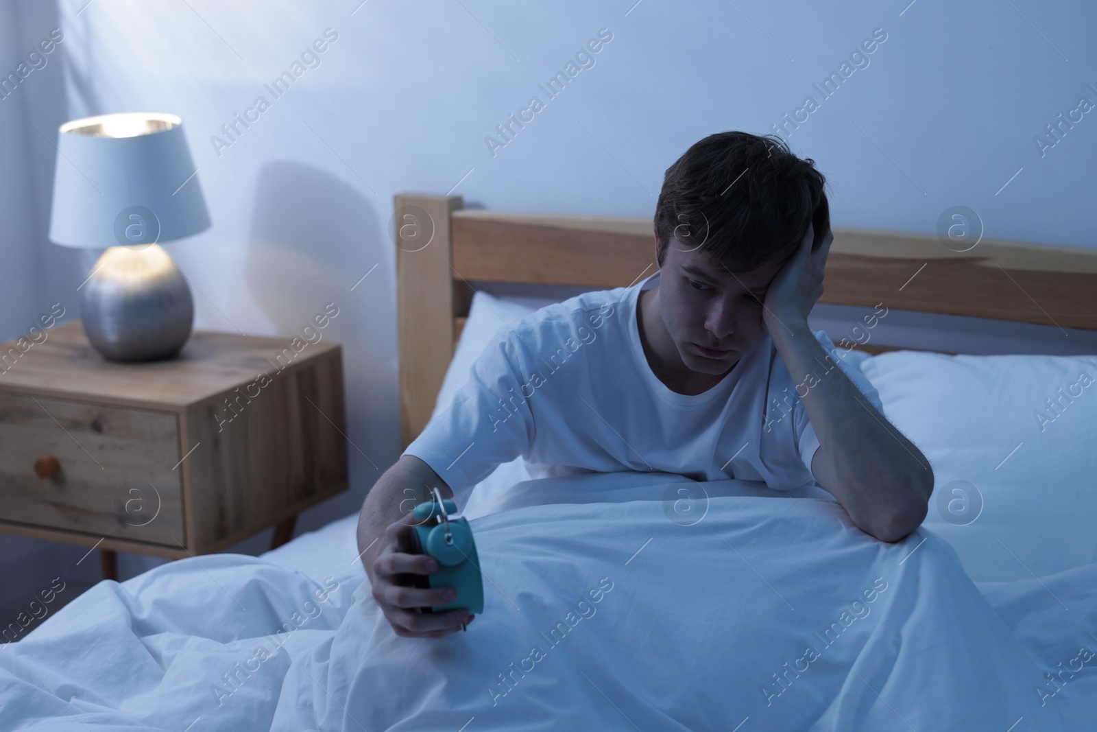 Frustrated man looking at alarm clock on bed at night. Insomnia problem Photo of Frustrated man looking at alarm clock on bed at night. Insomnia problem