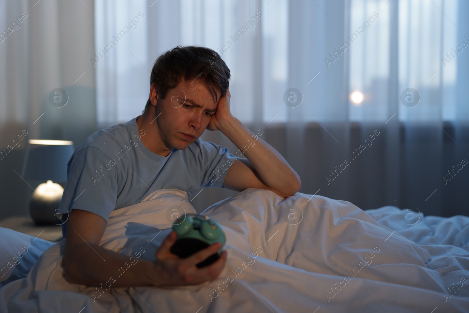 Frustrated man looking at alarm clock on bed at night. Insomnia problem Photo of Frustrated man looking at alarm clock on bed at night. Insomnia problem