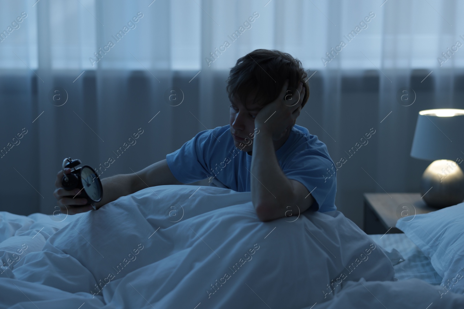 Frustrated man looking at alarm clock on bed at night. Insomnia problem Photo of Frustrated man looking at alarm clock on bed at night. Insomnia problem