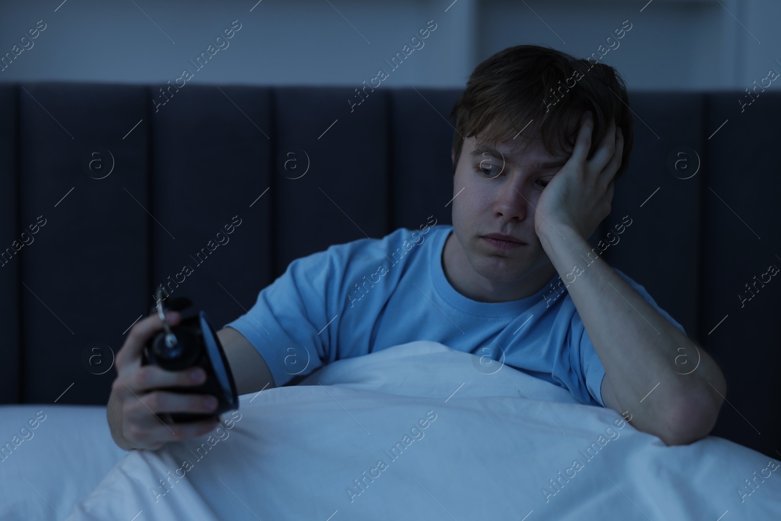 Frustrated man looking at alarm clock on bed at night. Insomnia problem Photo of Frustrated man looking at alarm clock on bed at night. Insomnia problem