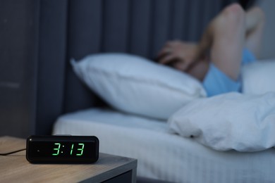 Photo of Man suffering from insomnia on bed indoors, focus on digital alarm clock