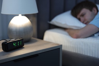 Photo of Man suffering from insomnia on bed indoors, focus on digital alarm clock