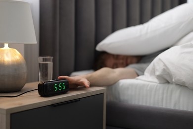 Photo of Man turning off digital alarm clock in bed at home, selective focus