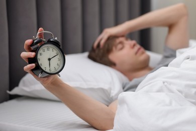 Photo of Sleepy man with alarm clock in bed indoors, selective focus