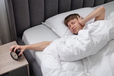 Photo of Sleepy man turning off alarm clock in bed indoors, above view