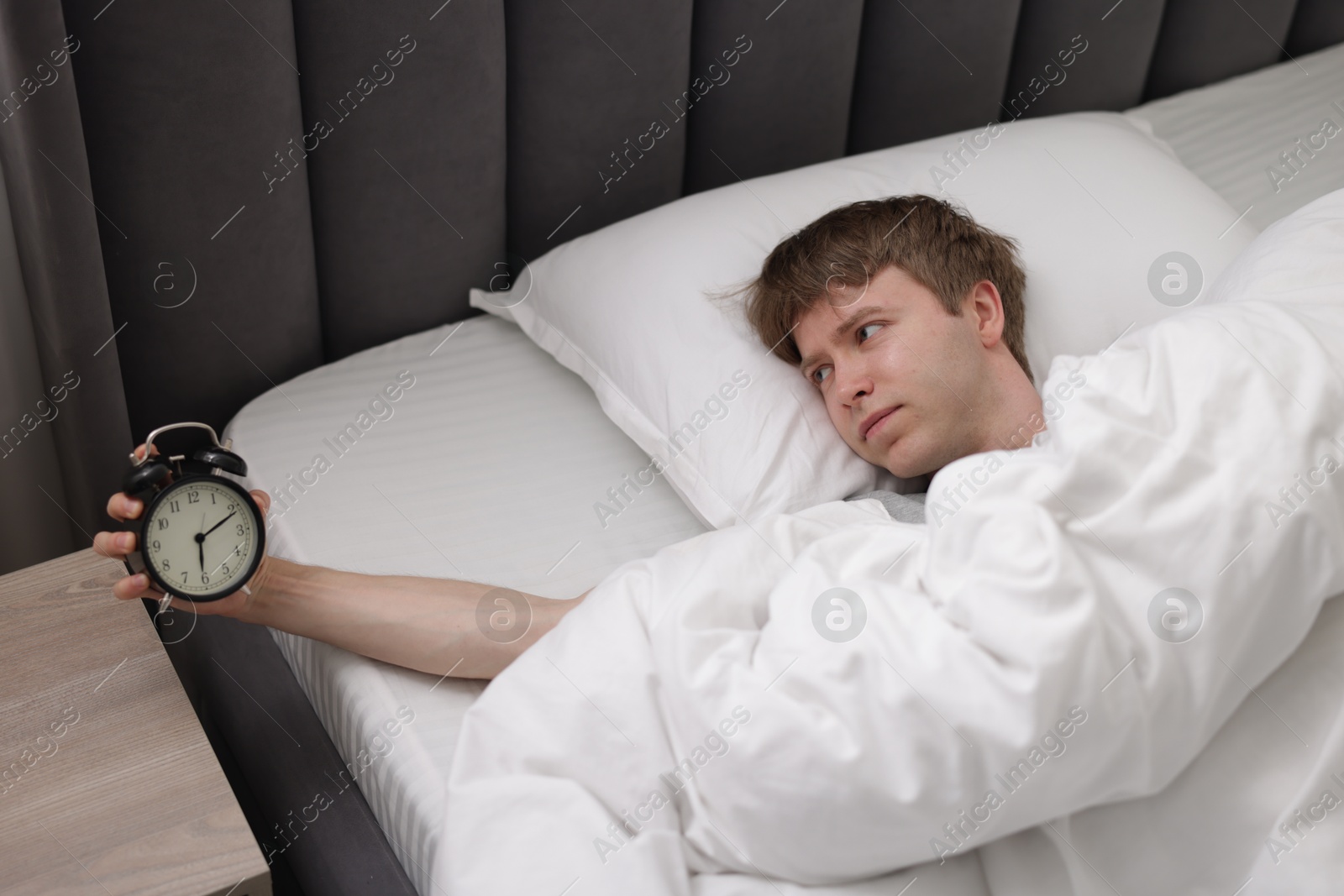 Sleepy man with alarm clock in bed indoors, above view Photo of Sleepy man with alarm clock in bed indoors, above view
