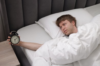 Photo of Sleepy man with alarm clock in bed indoors, above view