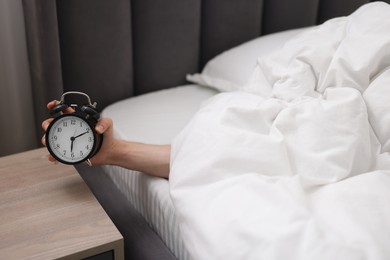 Photo of Sleepy man with alarm clock in bed indoors