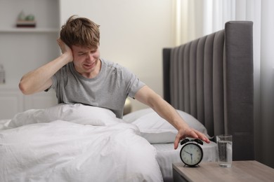 Photo of Frustrated man turning off alarm clock in bed indoors