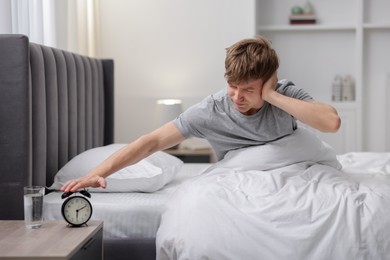Photo of Frustrated man turning off alarm clock in bed indoors