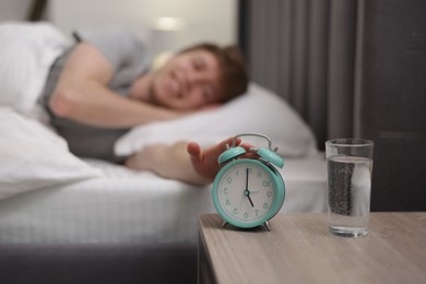 Photo of Happy man turning off alarm clock in bed indoors, selective focus