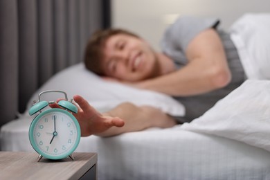 Photo of Happy man turning off alarm clock in bed indoors, selective focus