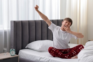 Photo of Young man stretching on bed indoors. Good morning